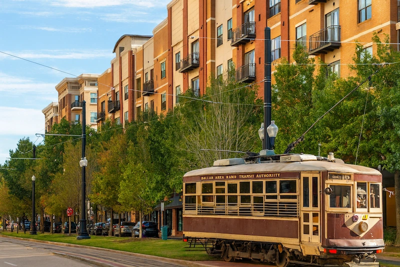 Dallas Uptown trolley on tree-lined street with modern red-brick apartments showcasing urban living and walkability