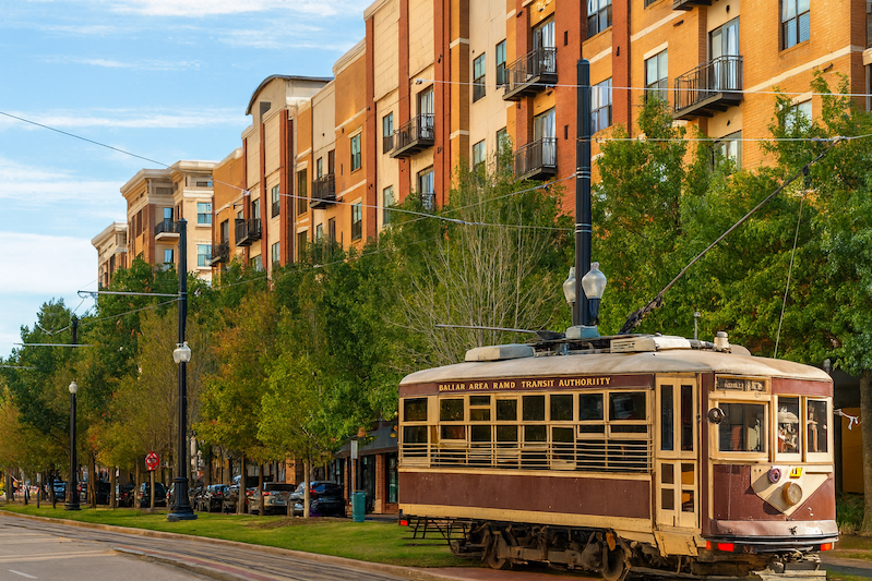 Dallas Uptown trolley on tree-lined street with modern red-brick apartments showcasing urban living and walkability